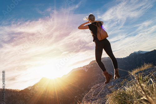Fototapeta Naklejka Na Ścianę i Meble -  Young blonde woman with backpack standing on the peak of mountain looking far away.  Alps scenery. Traveler concept.