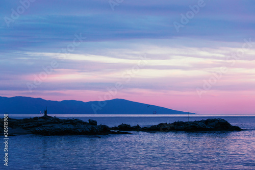 Rocky island silhouette in the sea during purple sunset.