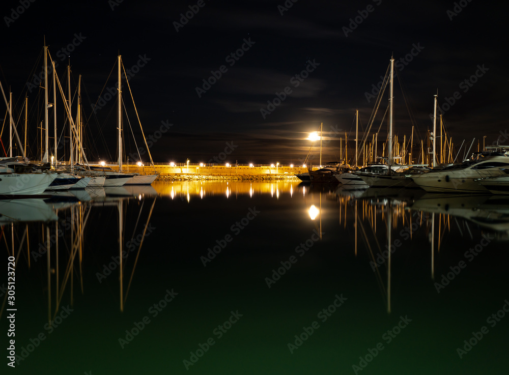 full moon in the marina of gandia with reflections in the water of the boats