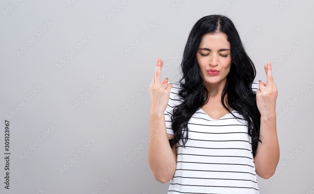Young woman crossing her fingers and wishing for good luck on a gray background Young woman crossing her fingers and wishing for good luck on a gray background