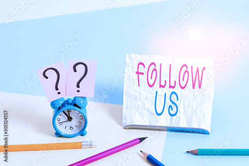 Writing note showing Follow Us. Business concept for To invite a demonstrating or group to join his company and take rules Mini size alarm clock beside stationary on pastel backdrop © Artur