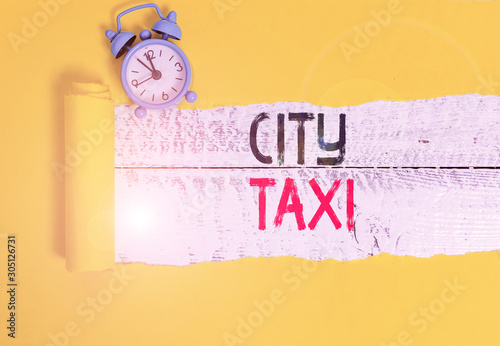 Conceptual hand writing showing City Taxi. Concept meaning type of vehicle for hire with a driver often for a nonshared ride Alarm clock and torn cardboard on a wooden classic table backdrop