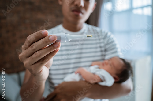 Father with baby newborn and thermometer at home