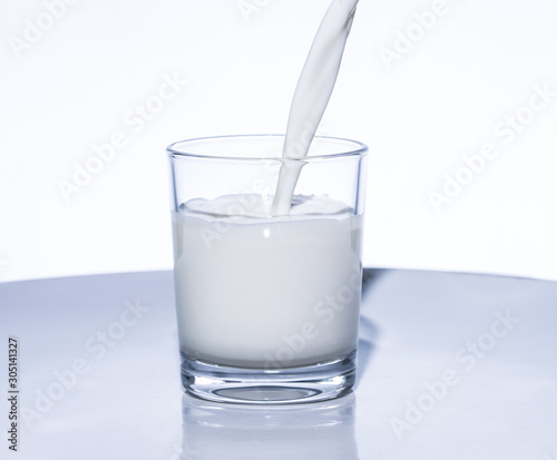 Milk is poured into a glass in front of white background. Concept: fresh milk