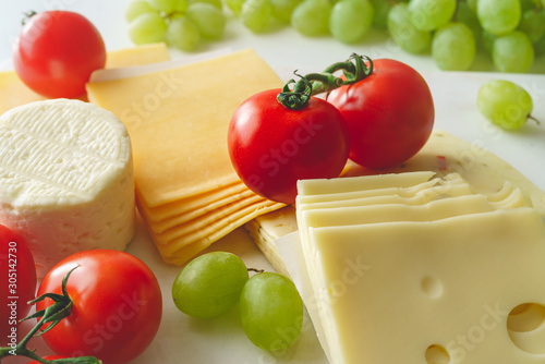 Variety of cheese served with tomatoes and green grape. Appetizer concept