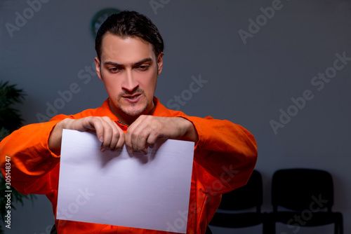 Young convict man sitting in dark room photo