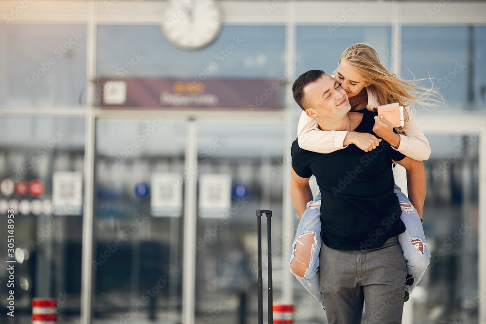 Couple in a airport. Beautiful blonde in a white jacket. Man in a black t-shirt Couple in a airport. Beautiful blonde in a white jacket. Man in a black t-shirt