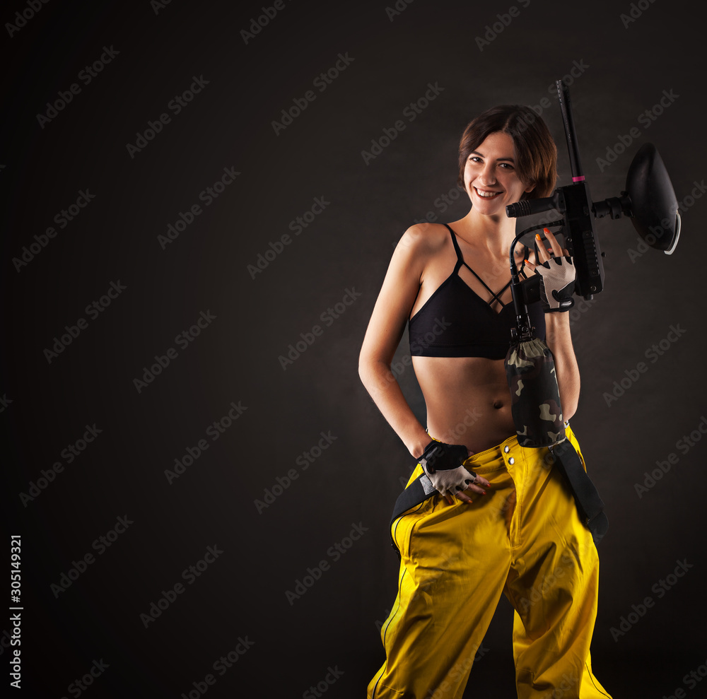 pretty woman in equipment with a paintball gun on a black background. Leisure pretty woman in equipment with a paintball gun on a black background. Leisure