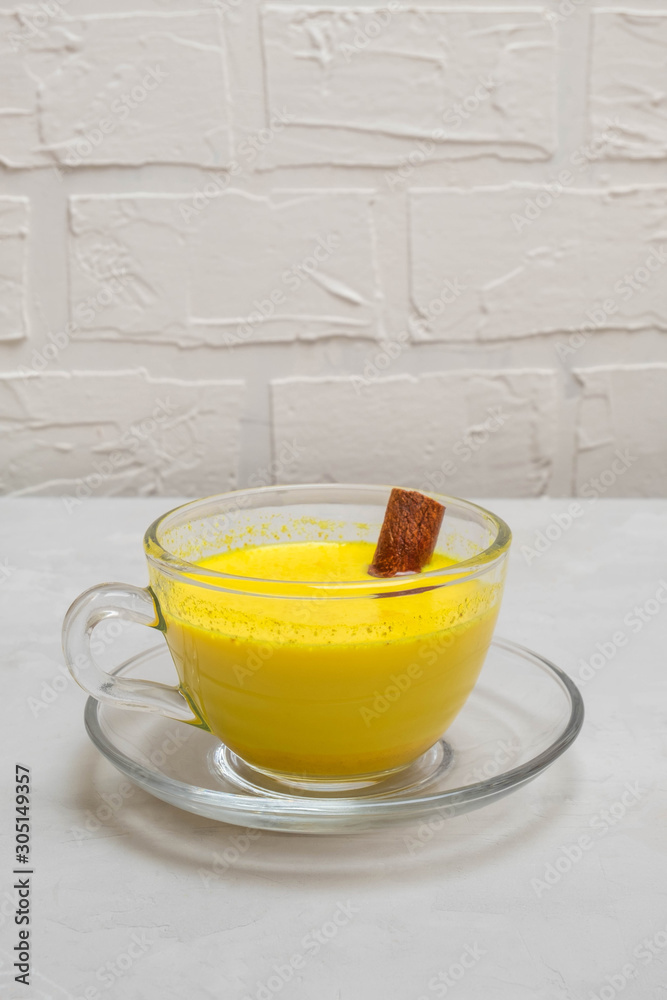 Traditional indian drink golden turmeric milk in a glass cup with cinnamon stick on neutral concrete table Traditional indian drink golden turmeric milk in a glass cup with cinnamon stick on neutral concrete table