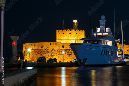 night Marina port Mandraki Rhodes island with a large yacht at the pier on background of the ancient fortification, the middle ages.