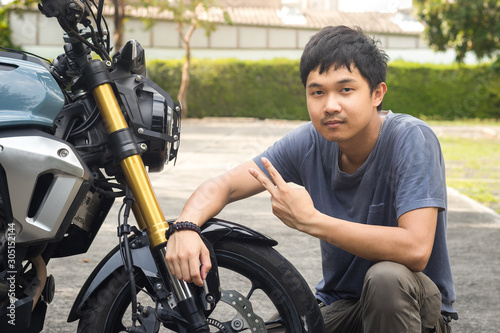 Attractive guy in t-shirt is looking at camera and smiling while sitting on the motorcycle. Motorcycle smile.