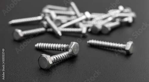 Heap of metal hex screws on black.