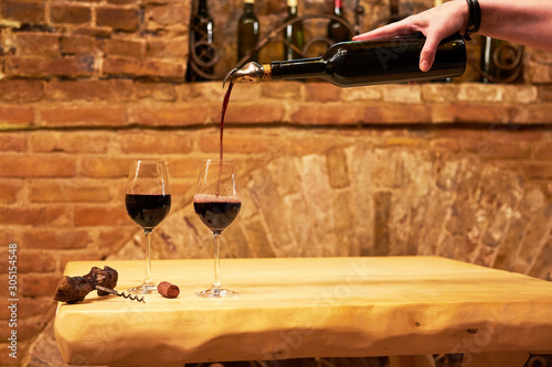 Obraz na płótnie Hand of a sommelier pouring red wine into long-stemmed wineglasses