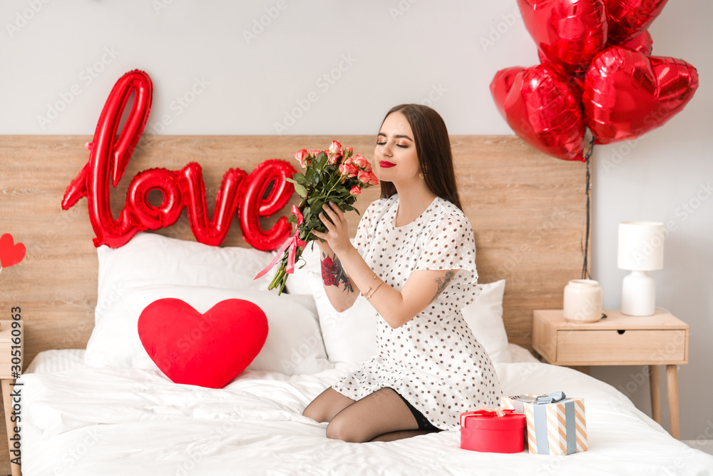 Beautiful young woman with gifts and flowers in bedroom. Valentine's Day celebration