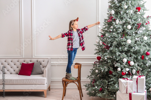 Happy little girl decorating Christmas tree at home
