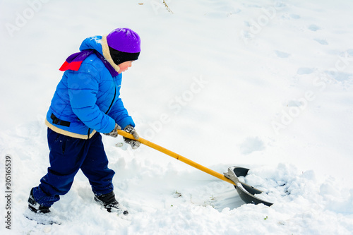 Smiling boy is carrying snow on a shovel, Child cleans the yard after a snowfall.