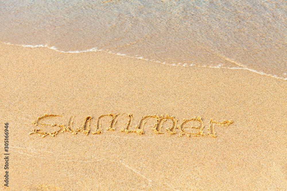 Text on a sunny beach. The word Summer is handwritten in sand, washed away by a sea wave. Vacation concept on a sandy beach. Copy space.