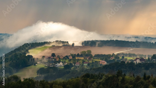 View from the Gamrig to the village Weißig in the saxon switzerland with rising fog and rain in the sunset