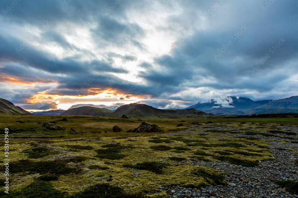 Mountain valley at sunset with cloudy sky. Stones covered with green moss in the foreground