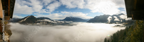 Panoramic view over a lake of fog and mist covering Lake Hallstatt and Bad Goisern. Some snow on the mountains is visible with blue skies.