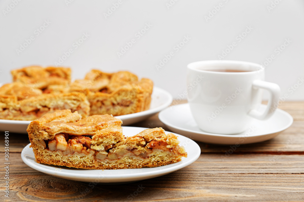 Homemade pie with apples and cinnamon and a cup of tea on white wooden table. Shallow focus. Homemade pie with apples and cinnamon and a cup of tea on white wooden table. Shallow focus.