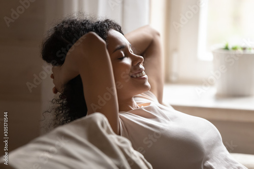 Happy biracial woman relax on couch with eyes closed photo