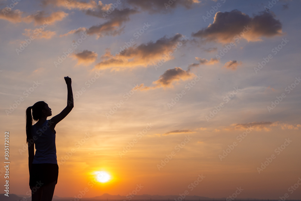 Strong, victorious and motivated young woman raising her fist up to the sunset sky. 