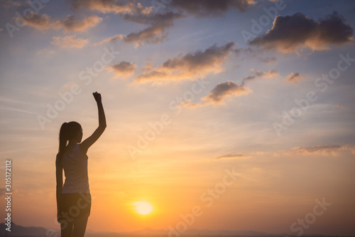 Strong, victorious and motivated young woman raising her fist up to the sunset sky. 