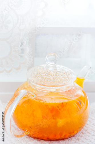 Sea buckthorn tea with orange in a glass teapot on a white background, selective focus