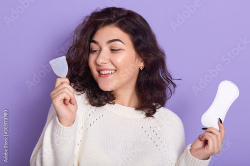 Woman holding menstrual cup and sanitary pad in hands. Feminine hygiene alternative product instead of tampon during her period. Menstruation, critical days, zero waste, eco, ecology concept. photo