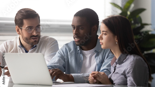 Serious multiethnic coworkers brainstorming in office using laptop © fizkes