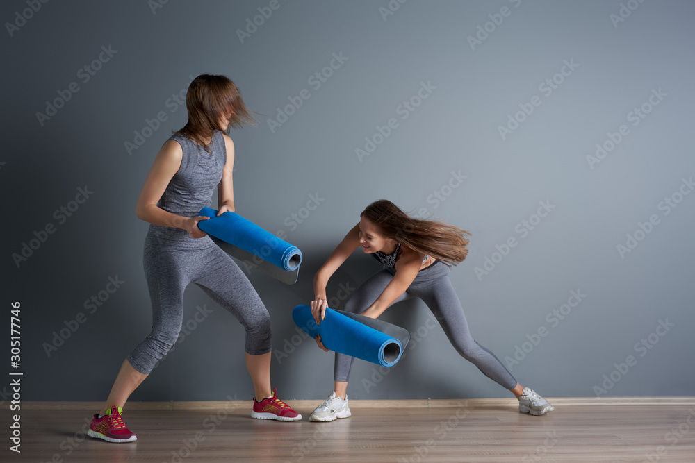 Fototapeta premium Sporty girls fighting twisted blue rugs against gray empty wall