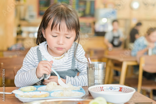 Little asian child girl with unhappy face while having lunch on table in restaurant,picky eater don't want to eat or Not hungry