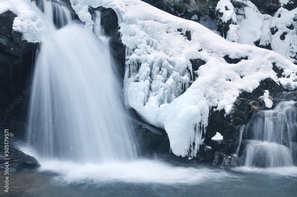Fototapeta premium Small active winter waterfall in mountains