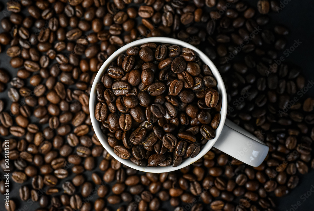 Coffee beans in a white coffee mug surrounded by coffee beans