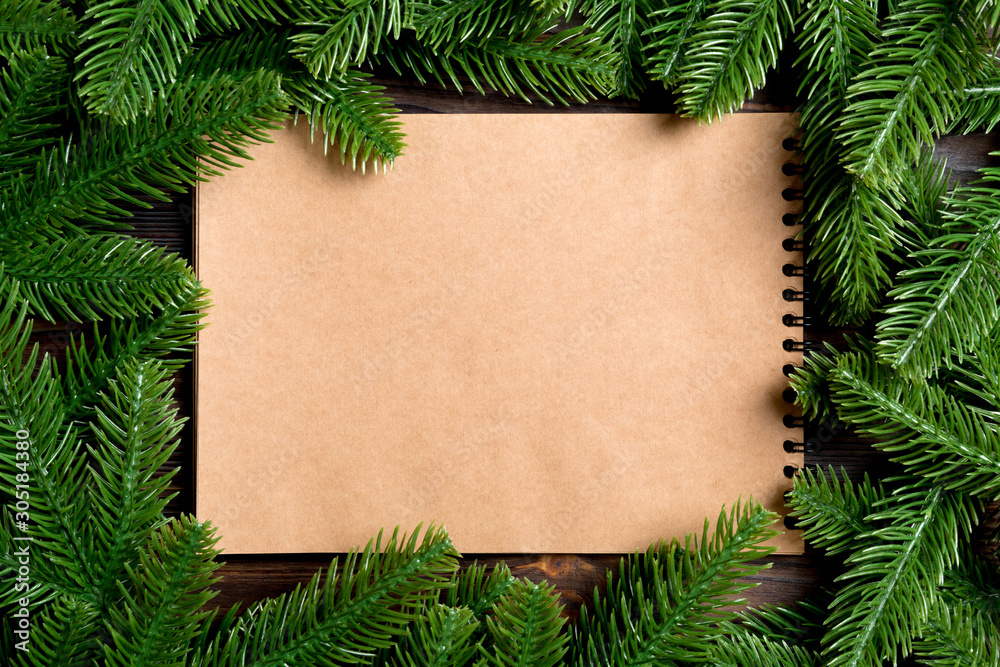 Top view of notebook made of craft paper decorated with a frame made of fir tree on wooden background. New Year time concept Top view of notebook made of craft paper decorated with a frame made of fir tree on wooden background. New Year time concept