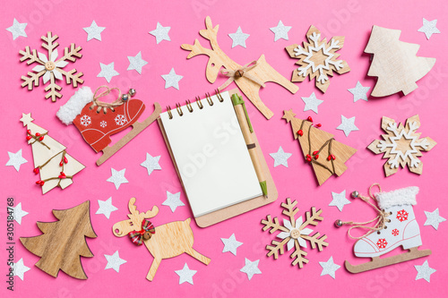 Top view of notebook, pink background decorated with festive toys and Christmas symbols reindeers and New Year trees. Holiday concept
