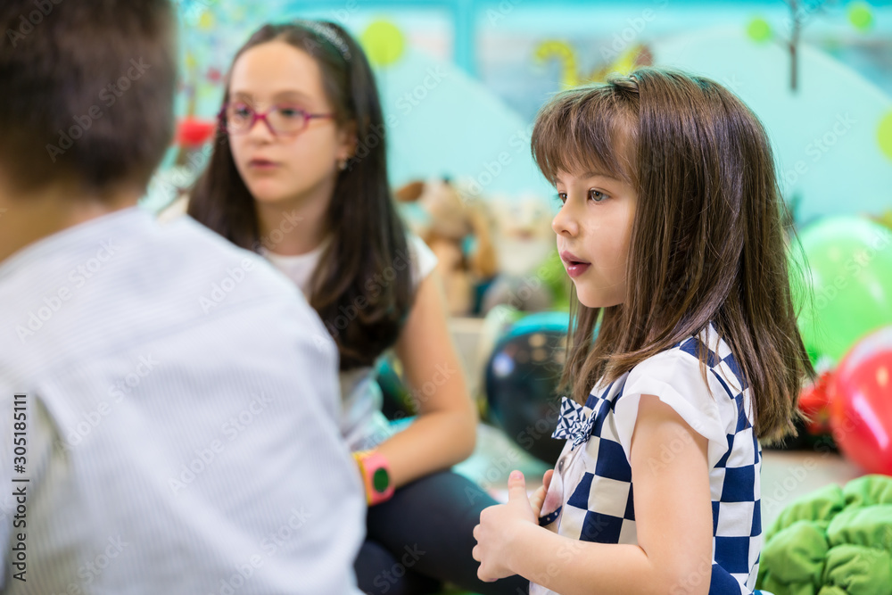 Shy girl looking at her playmates interacting in a modern kindergarten Shy girl looking at her playmates interacting in a modern kindergarten