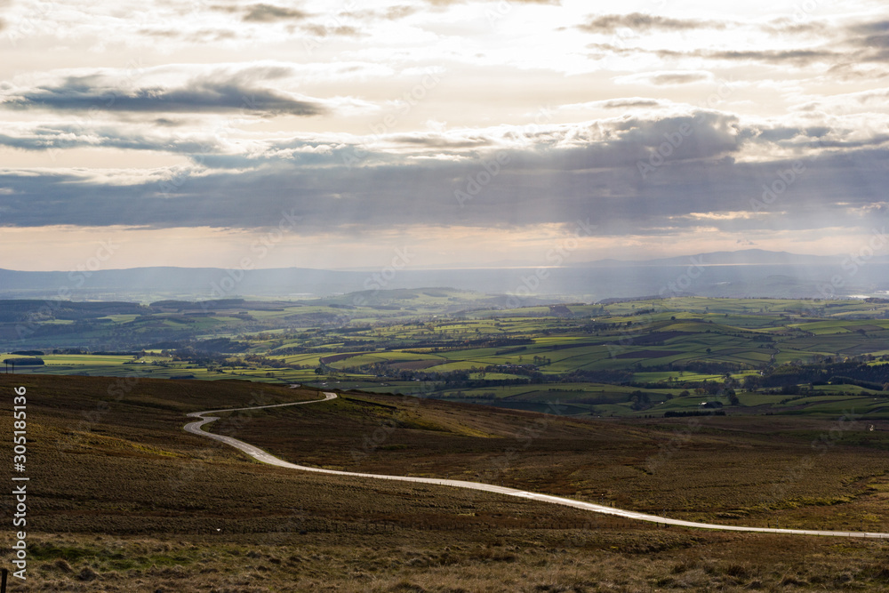 Cumbrian Landscape, Eden Valley, and distant Lake District hills taken from Hartside Top near Alston in the Pennines with rays from the setting sun breaking through the cloud