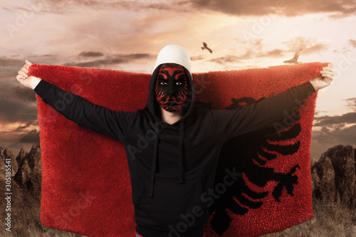 young man with painted albanian flag on face standing in front of rocky landscape and flying the fluffy albanian flag photo