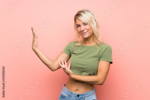 Young blonde woman over isolated pink background extending hands to the side for inviting to come