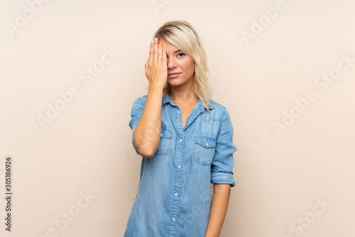 Young blonde woman over isolated background covering a eye by hand