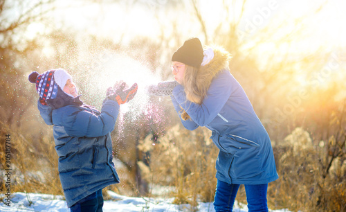 Children play in a snowy winter park at sunset. Throw snow and have fun. Winter fun. Holidays. © Tortuga