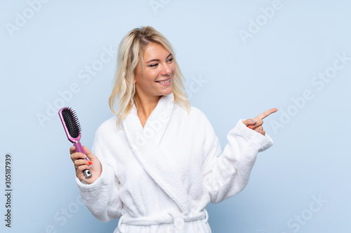 Young woman in a bathrobe with hair comb pointing to the side to present a product