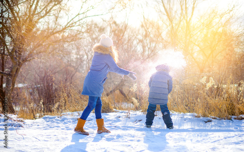 Children play in a snowy winter park at sunset. Throw snow and have fun. Winter fun. Holidays.