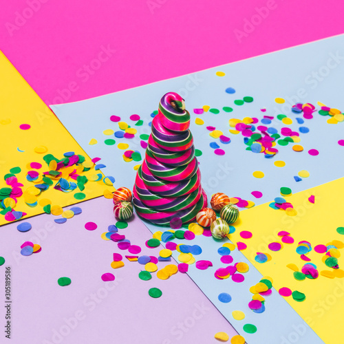 Candy Christmas treat in the shape of pine tree with little lollipops and confetti on geometric background. Minimalist. Happy holidays