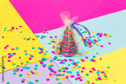 Candy Christmas treat in the shape of pine tree with little lollipops and confetti in plastic bag on geometric background. Minimalist. Happy holidays