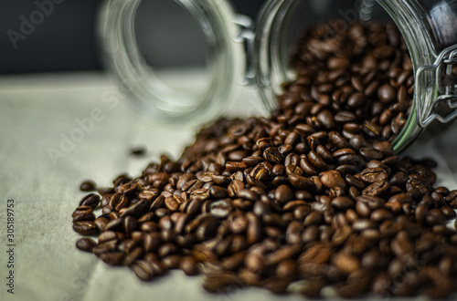 Fresh coffee beans pouring out of a glass coffee jar. 