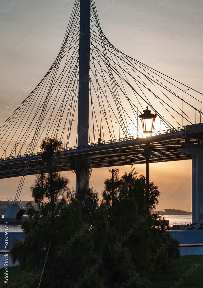 Obraz premium City landscape - view of the embankment, cable-stayed bridge and the bay on a frosty day at sunset, golden lighting