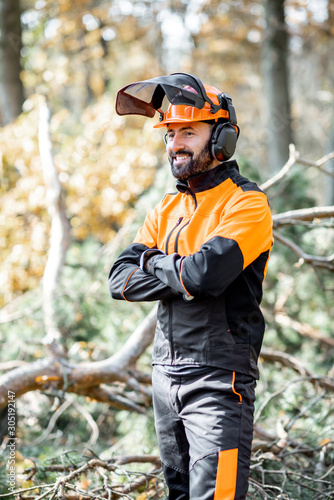 Portrait of a professional lumberman in harhat and protective workwear standing in the pine forest